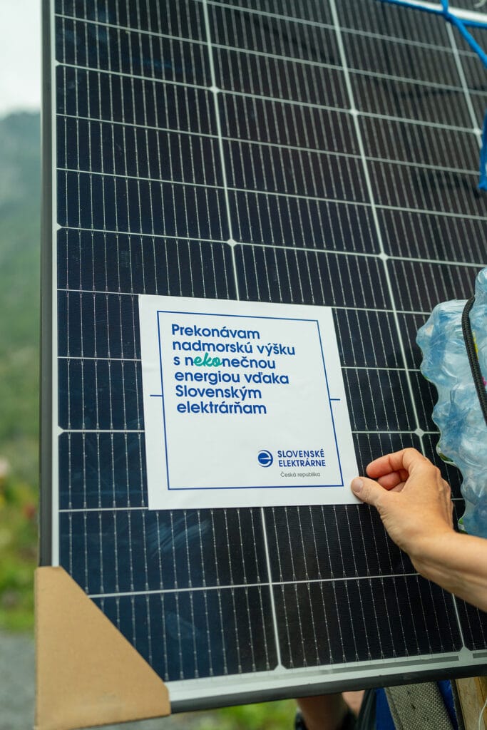 Detail solárního panelu; ruka drží papír s textem ve slovenštině a logem „Slovenské elektrárne – Česká republika“.